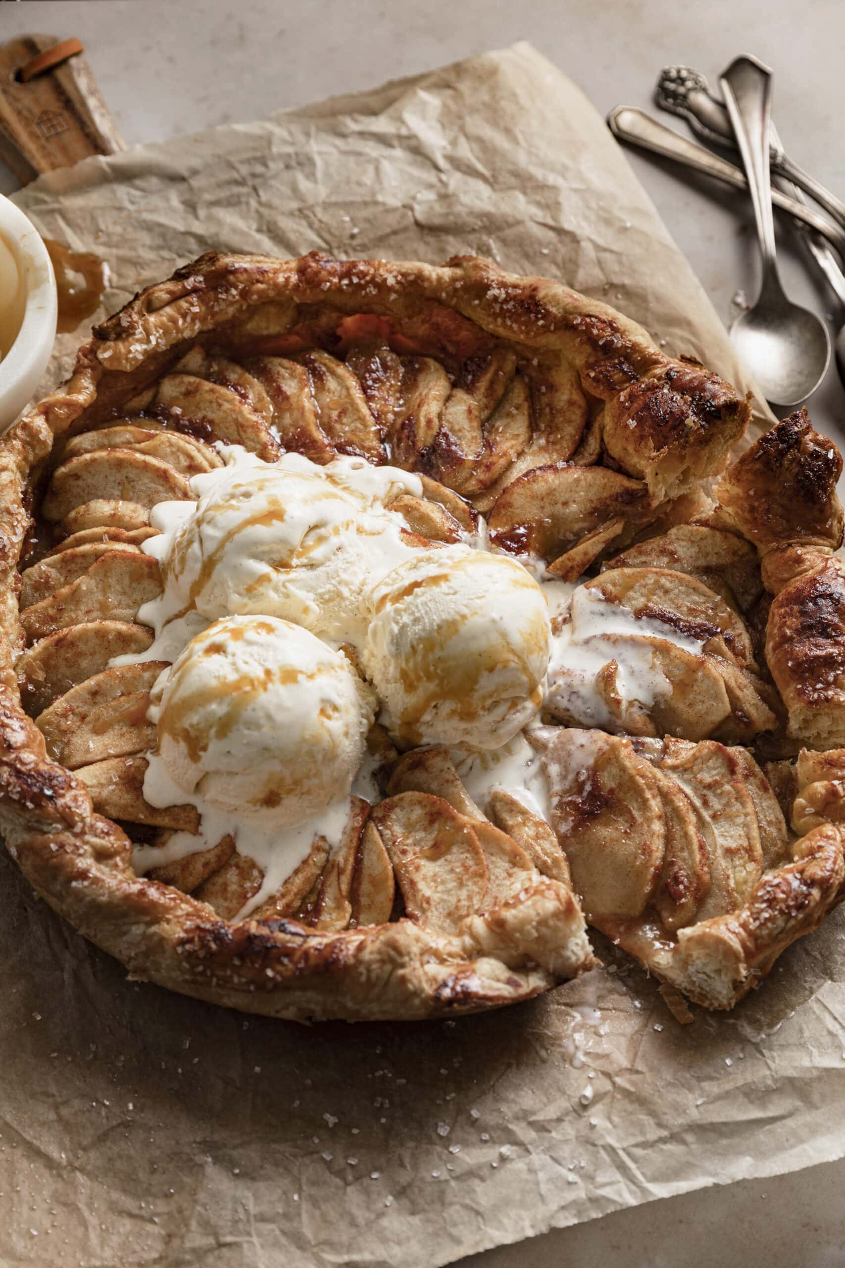 Apple Galette with puff pastry served with vanilla ice cream and caramel sauce, placed on parchment paper on a wood board.