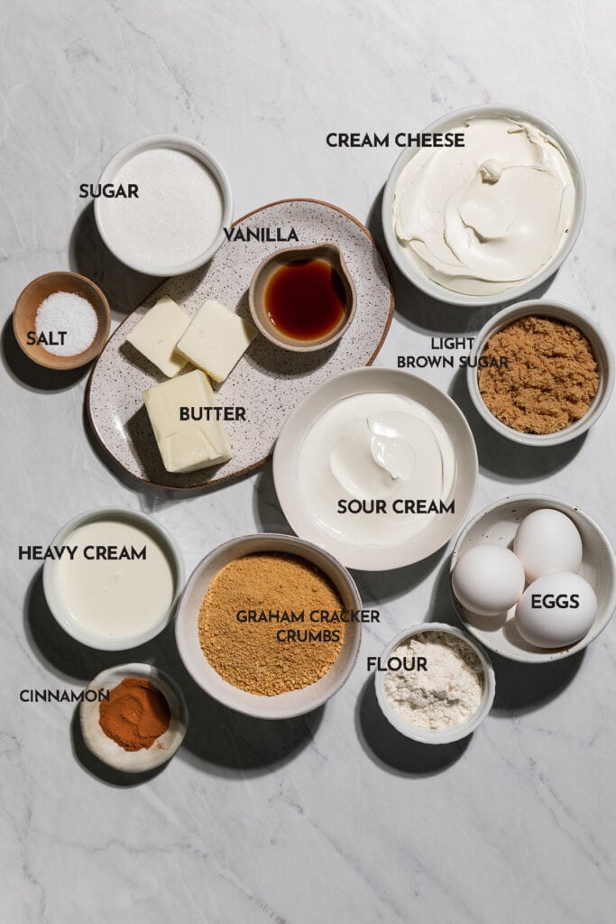 Ingredients to make Caramel Cheesecake: cream cheese, sour cream, sugar, flour, eggs, vanilla, graham cracker crumbs, butter, cinnamon, salt, brown sugar, heavy cream.