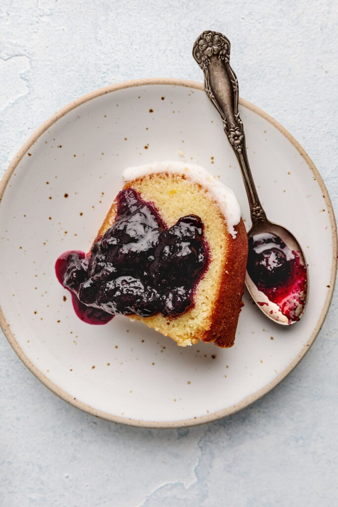 glazed lemon bundt cake slice with lemon icing and served with blueberry compote (or sauce)