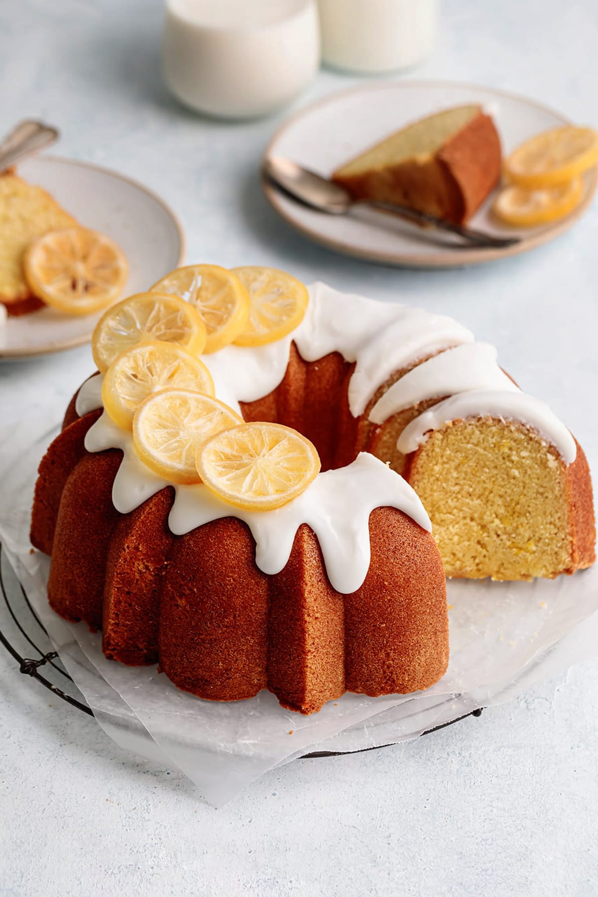 glazed lemon bundt cake with white lemon icing and dried lemons, cut with slices on plates.