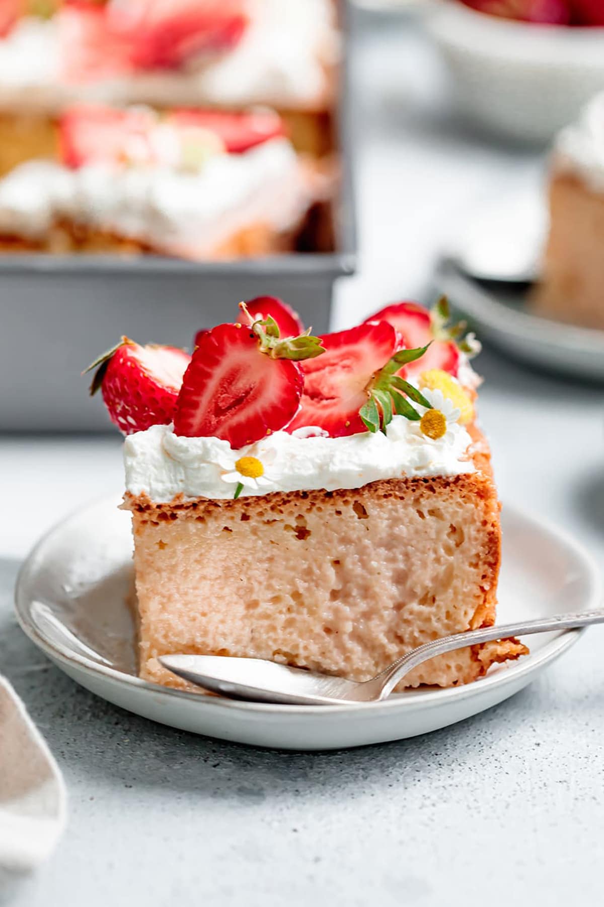 Strawberry Tres Leches cake slice, topped with whipped cream and sliced strawberries.